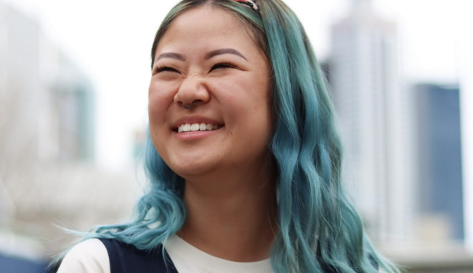 ID: Young writer Tiffany Ko is smiling slightly off camera. She has blue hair.